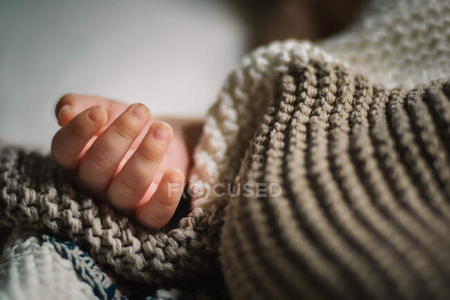 Крупним планом рука анонімної сплячої дитини лежить під м'якою в'язаною ковдрою в дитячій — стокове фото