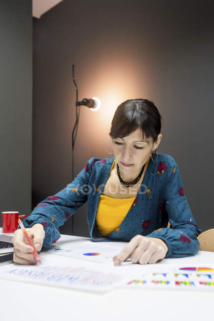 Donna d'affari in abito elegante prendere appunti di grafici mentre seduto alla scrivania in ufficio moderno — Foto stock