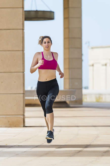 Женщина в спортивной одежде бежит по тропинке возле здания в городе — стоковое фото