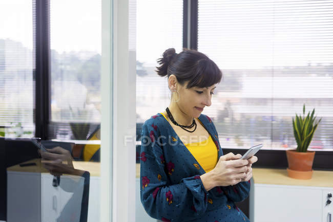 Улыбающаяся женщина-менеджер с помощью смартфона в современном офисе — стоковое фото