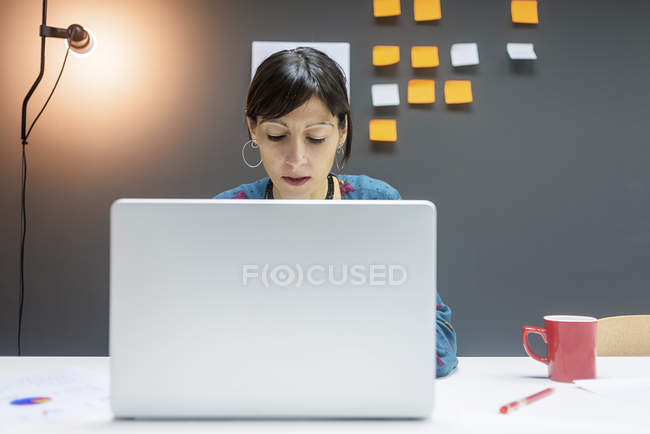 Empresária trabalhando no laptop enquanto sentado na mesa no escritório moderno — Fotografia de Stock