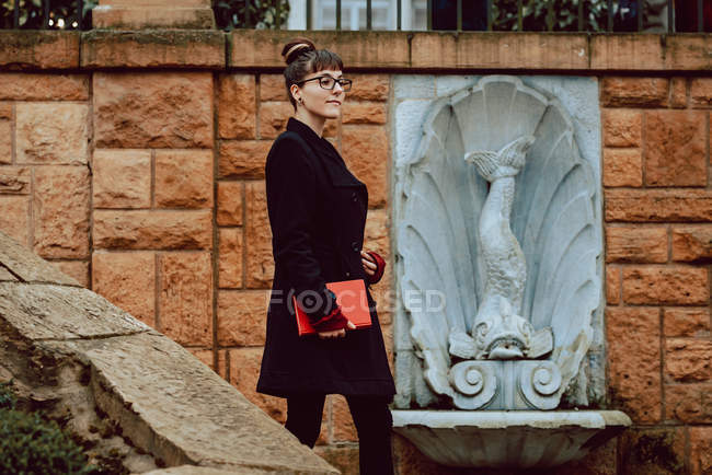 Junge elegante Frau mit Brille hält Buch in der Hand und steigt die Treppe hinunter — Stockfoto