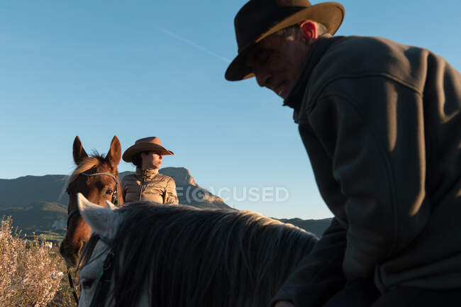 Homem e mulher montando cavalos contra o pôr do sol céu no rancho — Fotografia de Stock