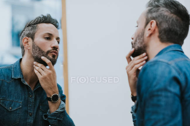 Reflection in mirror of handsome stylish male checking beard in salon — Stock Photo
