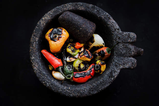 Delicious roasted vegetables in mortar on black background — Stock Photo