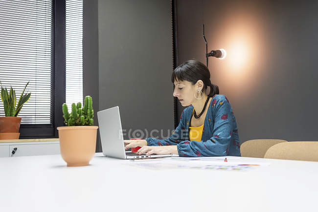 Fokussierte Geschäftsfrau arbeitet am Laptop, während sie im modernen Büro am Schreibtisch sitzt — Stockfoto
