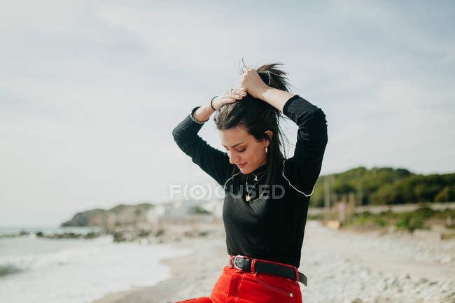 Femme élégante tenant les cheveux et regardant vers le bas sur la plage ensoleillée — Photo de stock