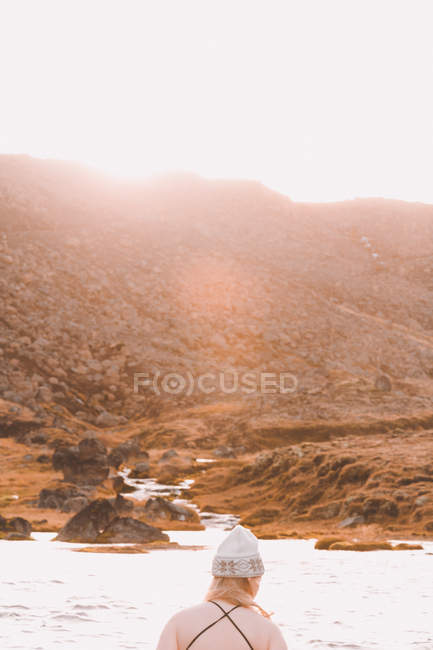 Visão traseira da mulher no chapéu perto da superfície da água com luz solar alta colina — Fotografia de Stock