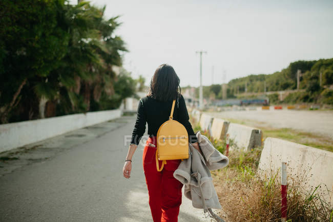 Visão traseira da jovem mulher na roupa da moda andando sobre fundo borrado de estacionamento — Fotografia de Stock