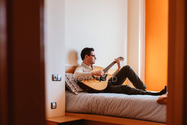 Hombre tocando la guitarra en la cama en casa - foto de stock