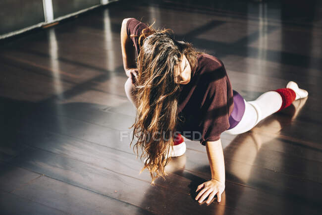 Bailarina de ballet segura calentándose en un estudio soleado mirando hacia otro lado con confianza. - foto de stock