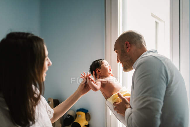 Hombre y mujer adultos que tocan y hablan suavemente con un adorable bebé recién nacido en una acogedora guardería en casa - foto de stock
