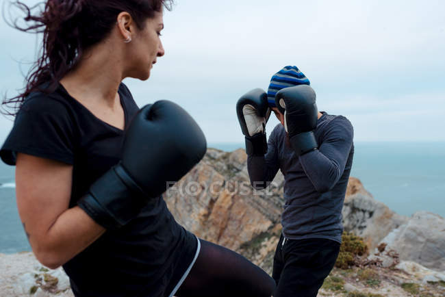 Homem e mulher em luvas de boxe batendo uns aos outros enquanto em pé no penhasco contra o mar e o céu — Fotografia de Stock