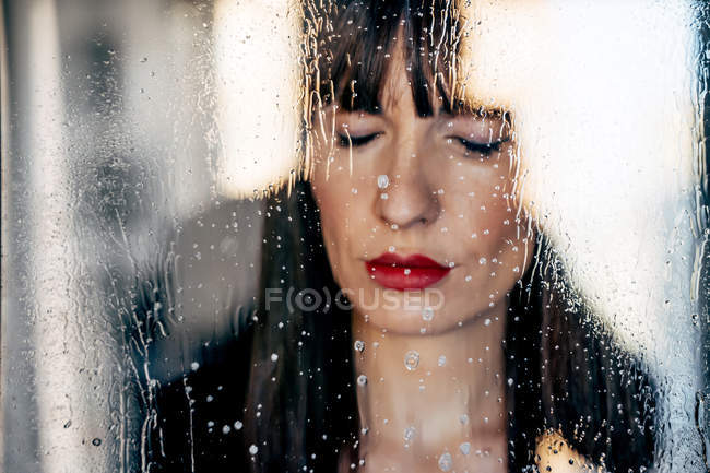 Attractive female with red lips with closed eyes behind transparent glass — Stock Photo