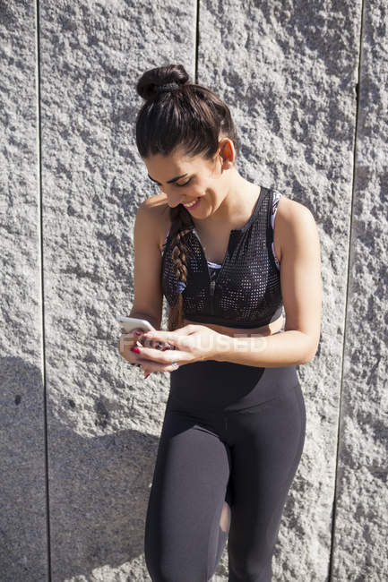 Брюнетка жінка спирається на гранітну стіну при використанні телефону і сміху — стокове фото