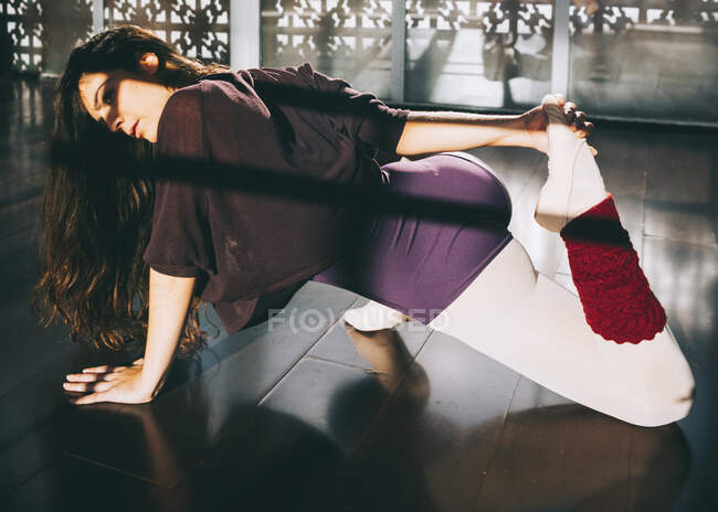 Bailarina calentando cuerpo flexible en estudio soleado. - foto de stock