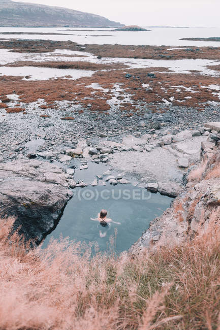 Frau ruht im Wasser nahe Klippe an trockener Küste zwischen Steinen — Stockfoto