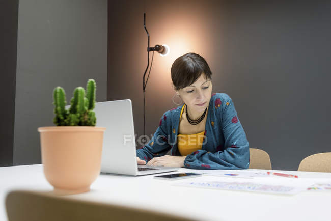 Businesswoman working with documents while sitting at desk with laptop in modern office — Stock Photo