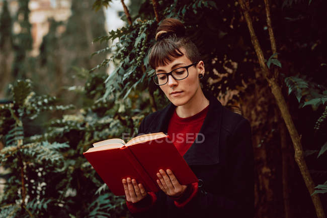Jovem atraente mulher elegante em óculos livro de leitura no jardim da cidade — Fotografia de Stock