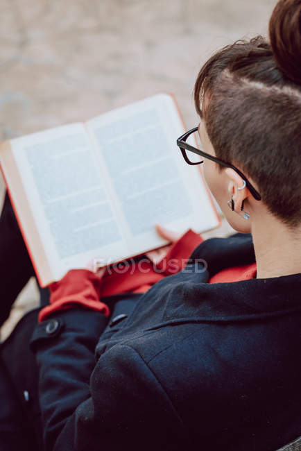 Молода стильна жінка в окулярах читає книгу на відкритому повітрі — стокове фото