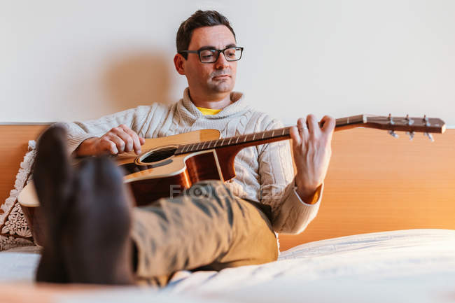 Homem tocando guitarra na cama em casa — Fotografia de Stock