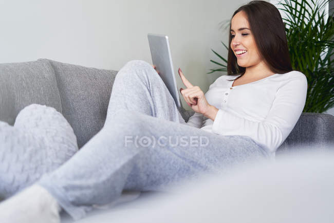 Young happy woman using digital tablet and resting on sofa at home — Stock Photo