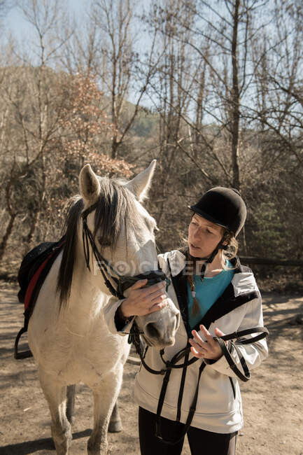 Жінка піклується про коня біля стайні після уроку в сонячний день на ранчо — стокове фото