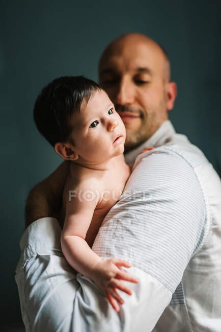 Bald adult man embracing sweet little baby while standing against gray background — Stock Photo