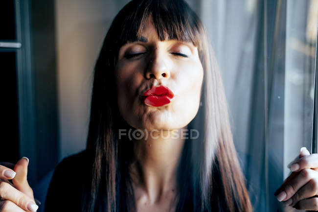 Приваблива жінка з червоними губами цілує чисте прозоре скло пристрасно — стокове фото