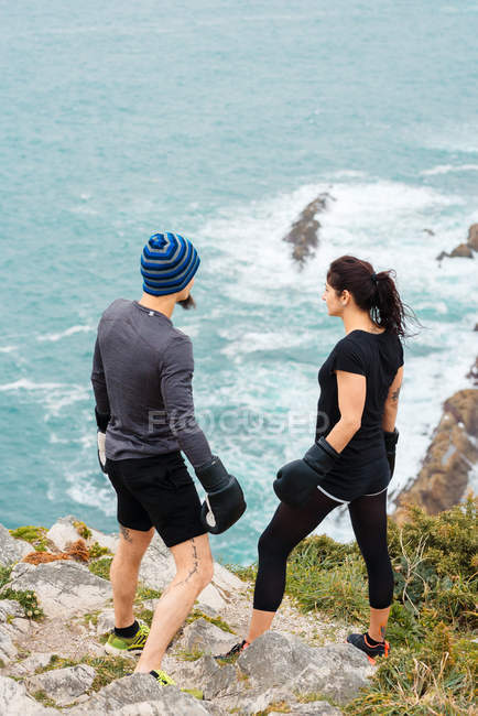 Man and woman in boxing gloves standing on cliff against sea — Stock Photo
