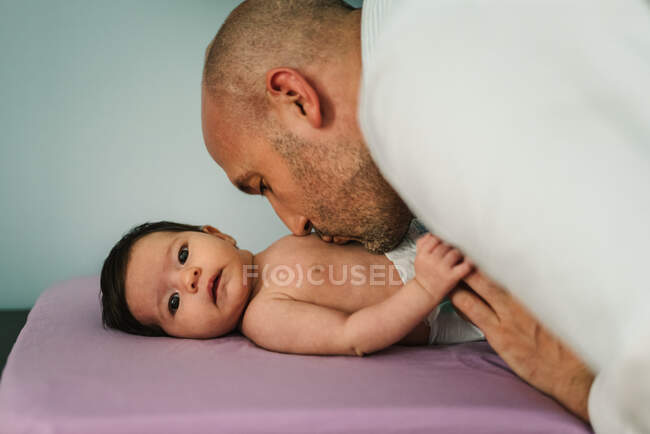 Glatzköpfiger erwachsener Mann küsst entzückendes Neugeborenes zu Hause im Bauch — Stockfoto