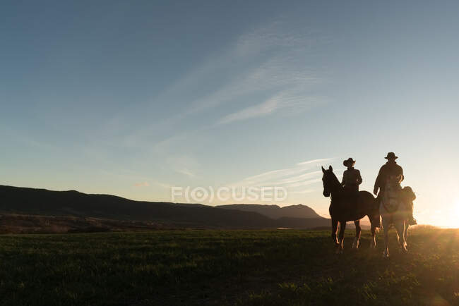 Homme et femme chevauchant des chevaux contre le soleil couchant ciel sur ranch — Photo de stock
