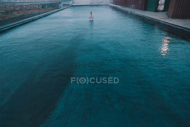 Mujer joven meditando en el agua de gran piscina en la naturaleza - foto de stock