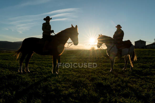 Man and woman riding horses against sunset sky on ranch — Stock Photo