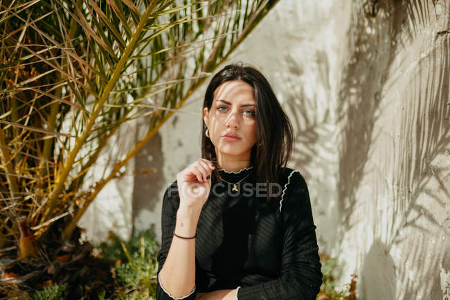 Ritratto di giovane donna seria in piedi vicino a foglie di palma tropicale sulla strada — Foto stock