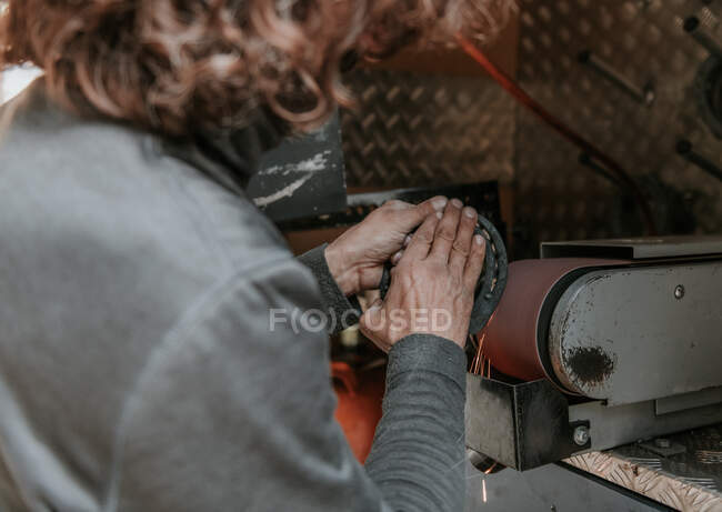Anonimo adulto fabbro finitura ferro di cavallo su smerigliatrice a nastro in officina — Foto stock