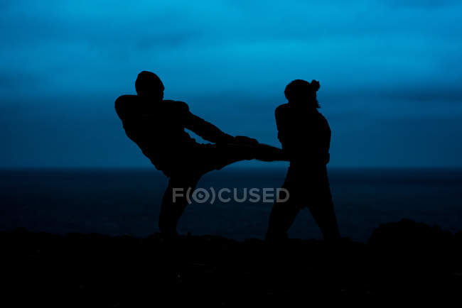 Silhuetas de lutadores anônimos praticando kickboxing contra o mar e céu escuro à noite no campo — Fotografia de Stock