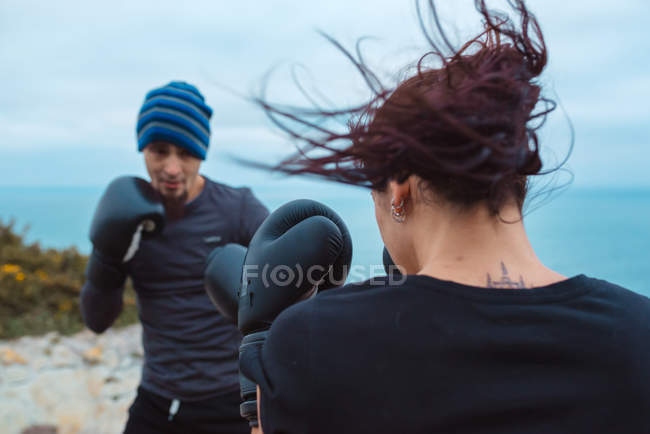 Homem e mulher em luvas de boxe batendo uns aos outros enquanto em pé na costa do mar — Fotografia de Stock