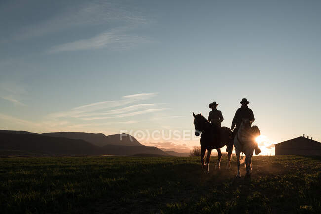 Мужчина и женщина едут на лошадях против закатного неба на ранчо — стоковое фото