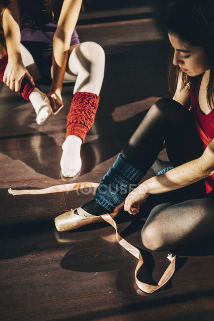 Young ballerinas wearing and lacing white pointe shoes in studio. — Stock Photo
