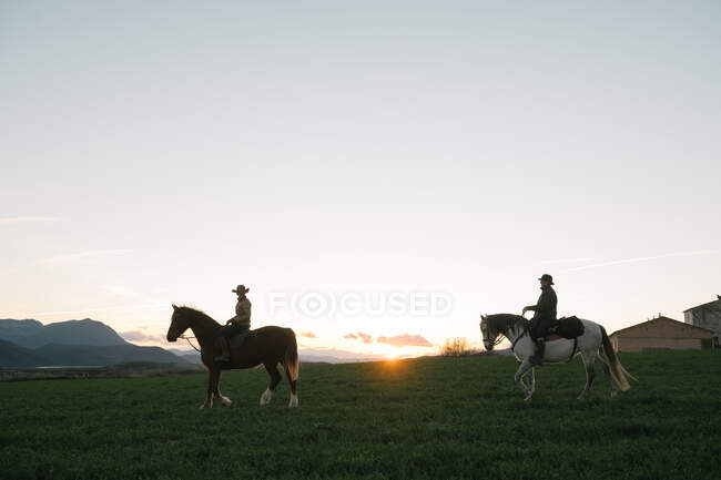 Homme et femme chevauchant des chevaux contre le soleil couchant ciel sur ranch — Photo de stock