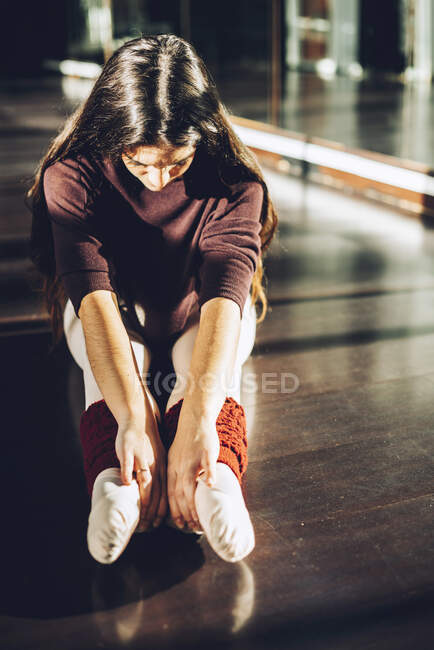 Ballerina sitting on floor in sunlight and bending forward warming up muscles. — Stock Photo