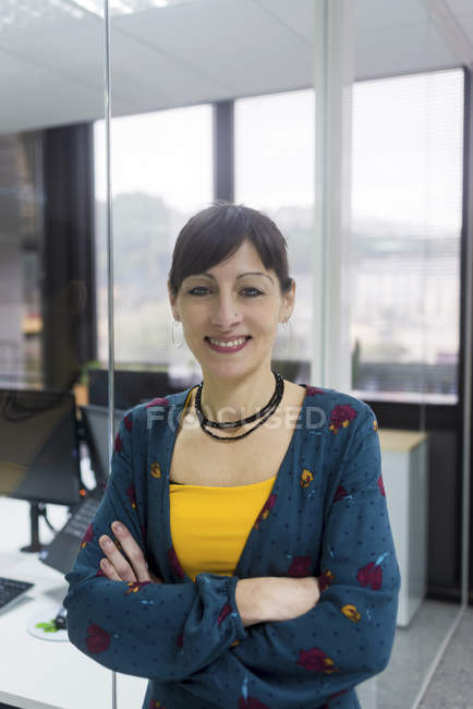 Porträt einer lächelnden Managerin, die an einer Glaswand in einem modernen Büro steht — Stockfoto