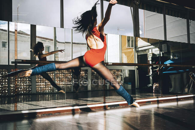 Back view of young slim ballerina jumping above ground in studio flexing legs. — Stock Photo