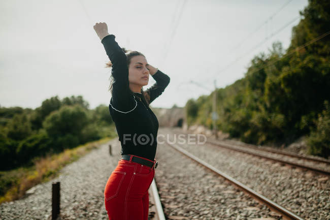 Mulher bonita com olhos fechados em roupa elegante posando no fundo borrado de trilhos — Fotografia de Stock