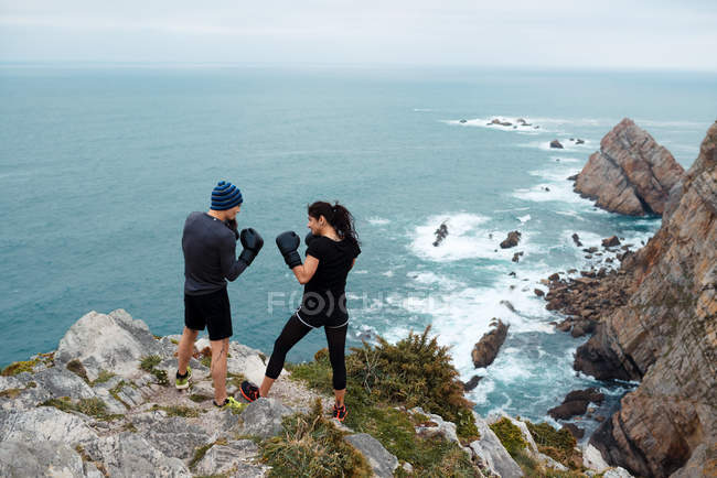 Homem e mulher em luvas de boxe em pé no penhasco contra o mar — Fotografia de Stock