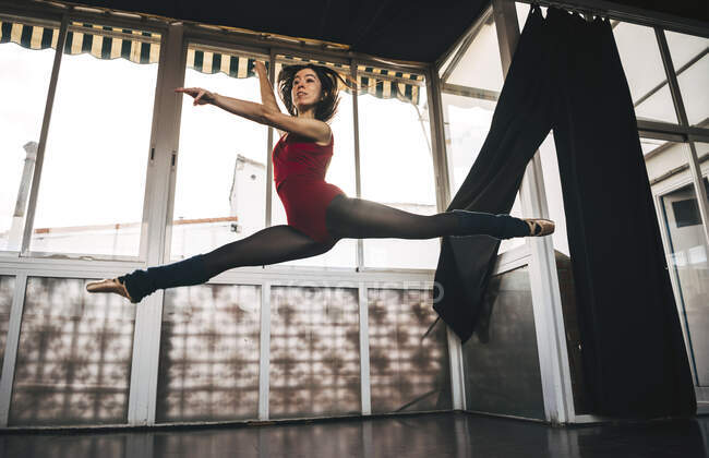 Young slim ballerina jumping above ground in studio flexing legs. — Stock Photo