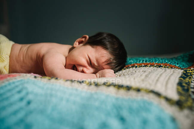 Симпатичный ребенок без рубашки лежит на теплом трикотажном одеяле и громко плачет в уютной детской — стоковое фото