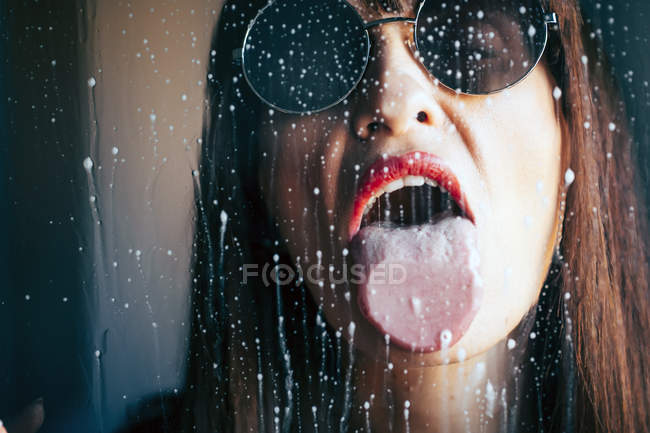 Mulher atraente com batom vermelho lambendo gotas líquidas de vidro transparente — Fotografia de Stock