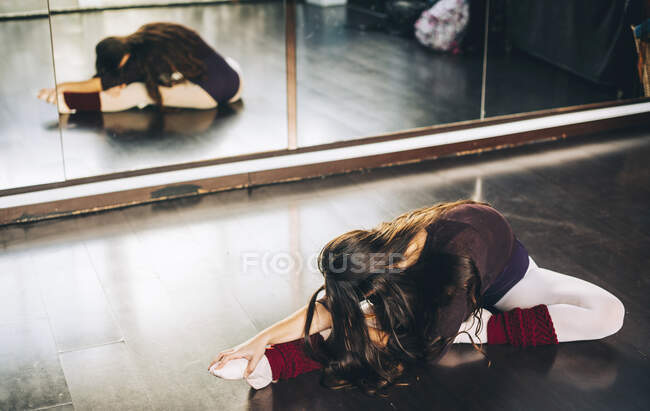 Young brunette in bodysuit sitting on floor in studio and flexing legs. — Stock Photo